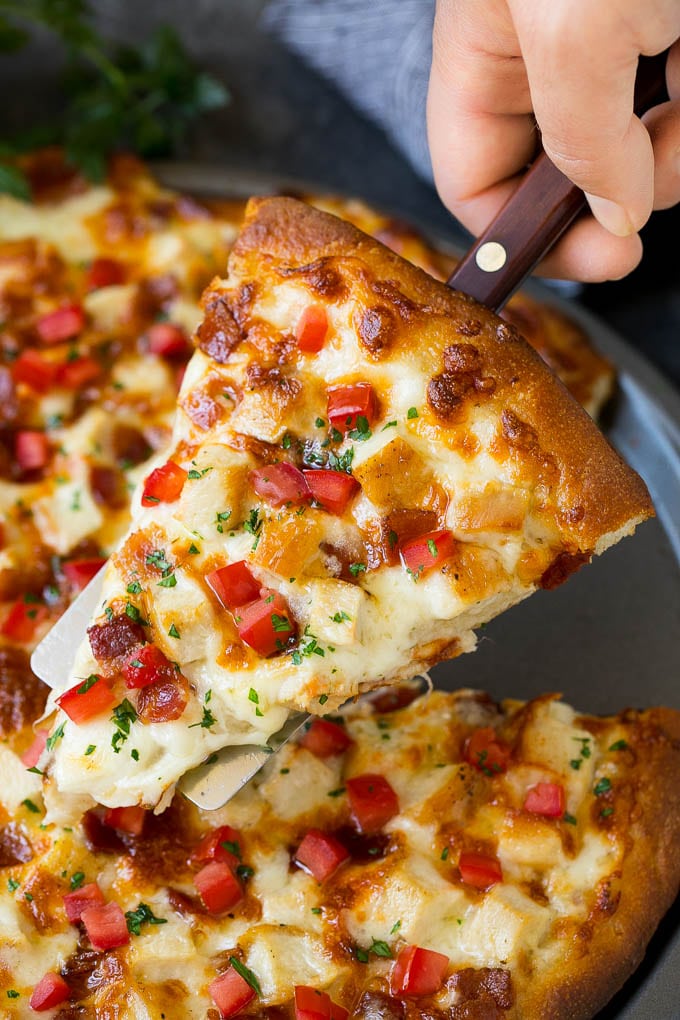 Chicken Alfredo Pizza Recipe #pizza #chicken #bacon #dinner #jonep A hand holding a spatula with a piece of chicken Alfredo pizza on it.