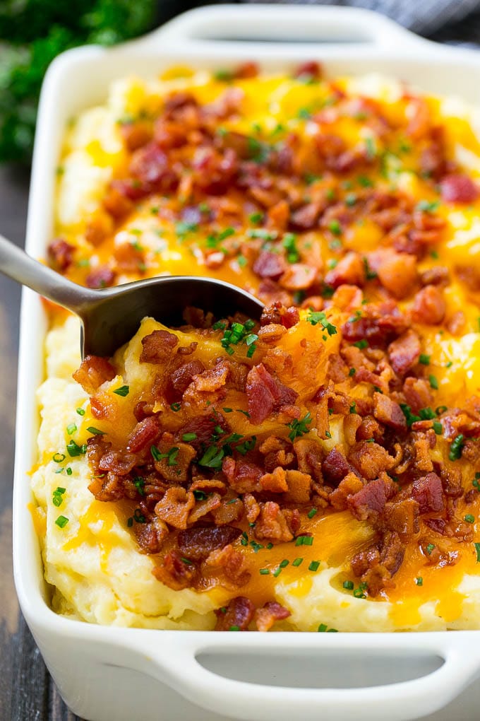 Loaded Mashed Potato Casserole Recipe | Loaded Potatoes | Bacon Mashed Potatoes | Thanksgiving Mashed Potatoes #potatoes #bacon #cheese #casserole #Thanksgiving #dinner #jonep A dish of loaded mashed potato casserole with a serving spoon in it.