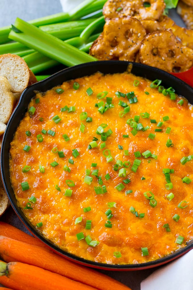 Buffalo Ranch Chicken Dip | Buffalo Chicken Dip | Baked Buffalo Dip | Cheesy Buffalo Dip #buffalowings #buffalochicken #dip #lowcarb #appetizer #jonep Buffalo ranch chicken dip topped with melted cheese and green onions, surrounded by vegetables, pretzels and baguette slices.