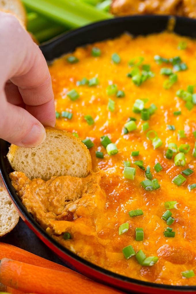 Buffalo Ranch Chicken Dip | Buffalo Chicken Dip | Baked Buffalo Dip | Cheesy Buffalo Dip #buffalowings #buffalochicken #dip #lowcarb #appetizer #jonep Baked buffalo chicken dip with a baguette slice scooping some out.