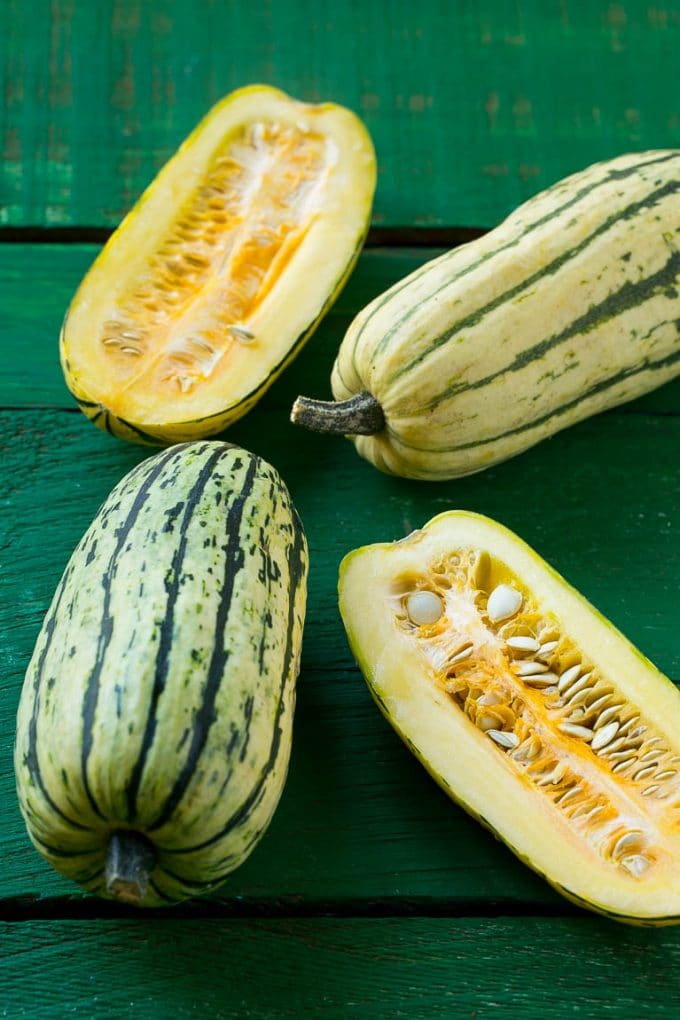 Brown Sugar Delicata Squash Recipe | Roasted Squash | Delicata Squash | Winter Squash Recipe #squash #wintersquash #brownsugar #sidedish #delicatasquash #dinner #jonep Raw delicata squash on a green board.