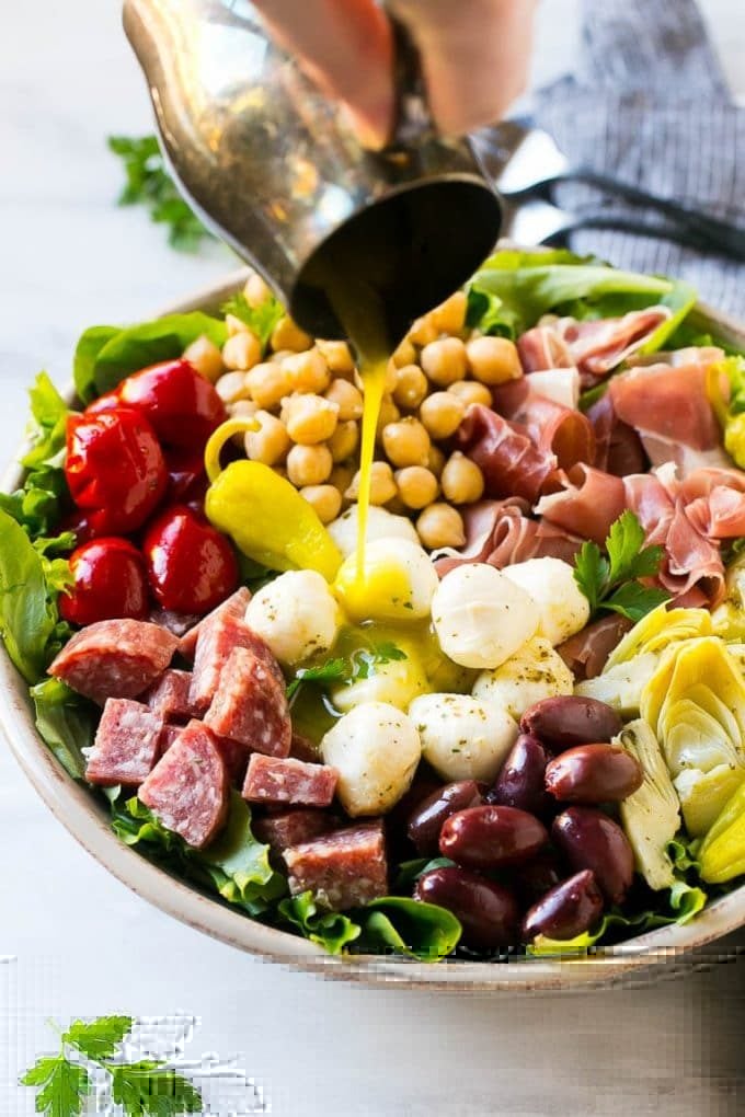 Antipasto Salad Recipe | Italian Salad | Main Course Salad | Antipasto Recipe #salad #salami #italianfood #dinner #lunch #jonep A pitcher of dressing being poured over antipasto salad.