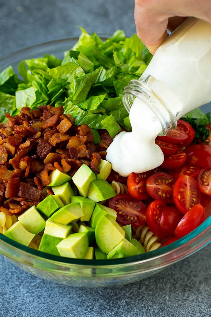 BLT Pasta Salad Recipe | Easy Pasta Salad | Bacon Pasta Salad #salad #pasta #blt #bacon #avocado #dinner #jonep Ranch dressing being poured over tomatoes, lettuce, bacon and avocado.