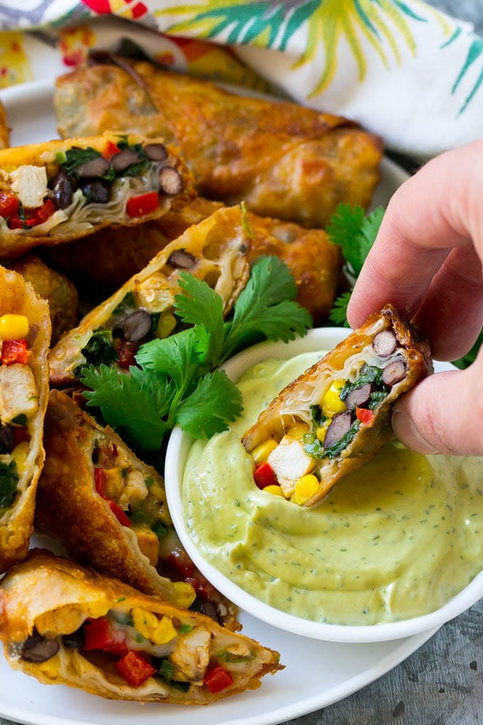 Southwestern Egg Rolls Recipe | Easy Egg Roll Recipe | Mexican Appetizer | Egg Roll Recipe | Southwest Egg Rolls #eggrolls #appetizer #chicken #snack #jonep A southwestern egg roll being dipped into avocado sauce.