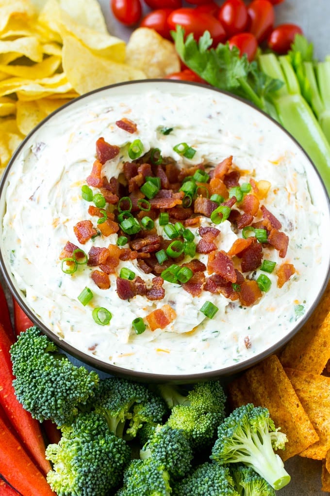 Bacon Ranch Dip Recipe | Homemade Ranch Dip | Easy Dip Recipe | Cheddar Ranch Dip #ranch #ranchdip #bacondip #dip #snack #jonep #baconranchdip A bowl of creamy bacon cheddar ranch dip surrounded by vegetables and chips.