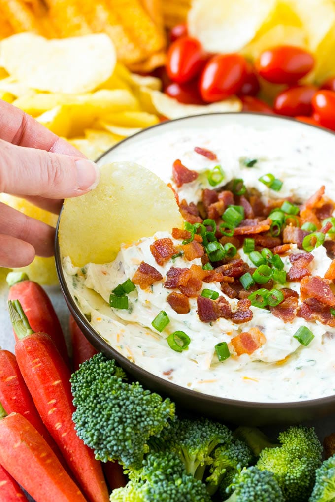 Bacon Ranch Dip Recipe | Homemade Ranch Dip | Easy Dip Recipe | Cheddar Ranch Dip #ranch #ranchdip #bacondip #dip #snack #jonep #baconranchdip A hand scooping up bacon ranch dip with a potato chip.