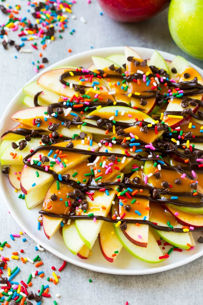 Apple Nachos Recipe | After School Snack | Caramel Apples #apple #apples #caramelapple #snack #dessert #jonep A plate of sliced apple nachos topped with caramel and chocolate sauces, rainbow sprinkles and mini chocolate chips