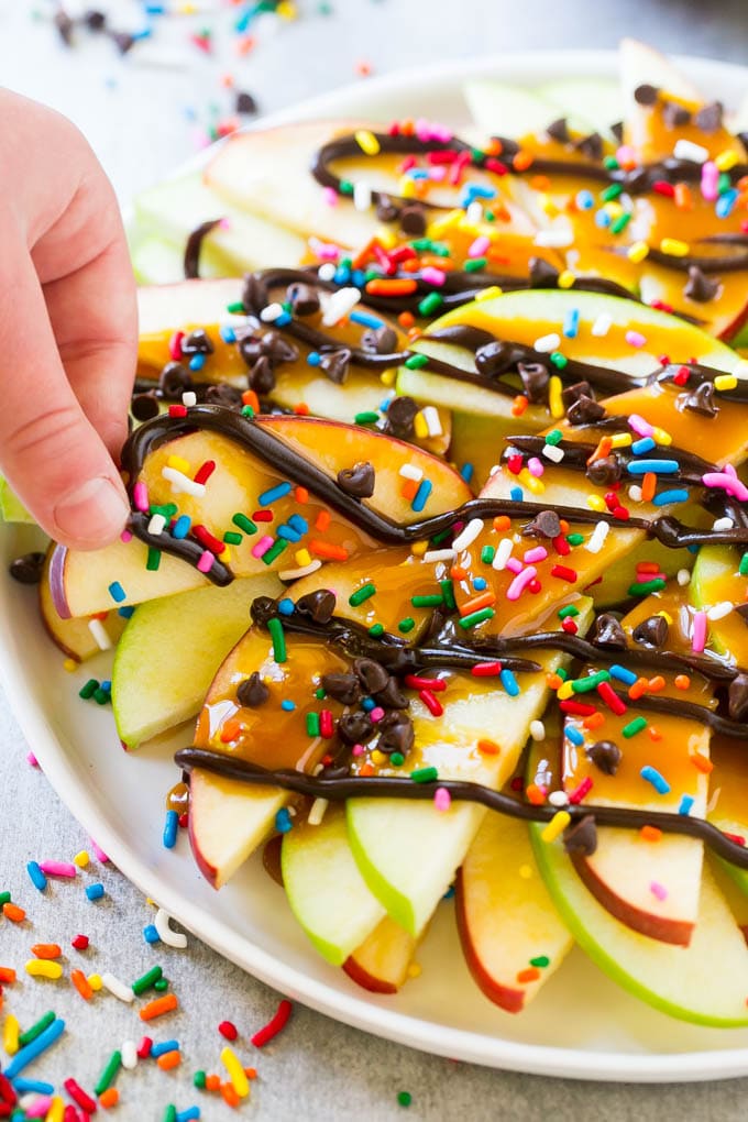 Apple Nachos Recipe | After School Snack | Caramel Apples #apple #apples #caramelapple #snack #dessert #jonep A plate of caramel apple nachos with a hand reaching out to take one.