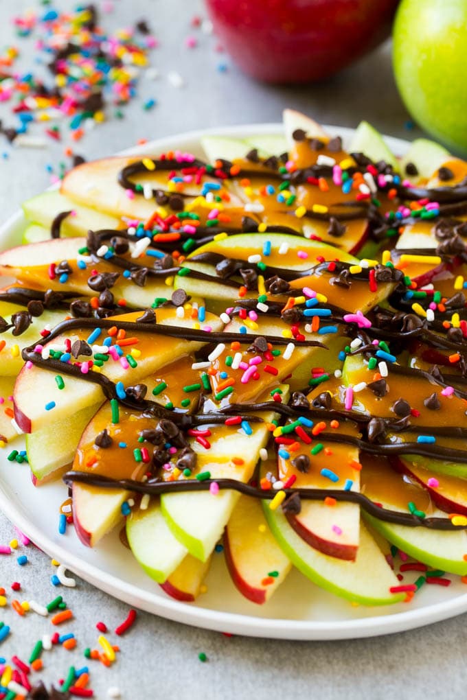 Apple Nachos Recipe | After School Snack | Caramel Apples #apple #apples #caramelapple #snack #dessert #jonep A plate of red and green sliced apples drizzled with caramel and chocolate, then topped with rainbow sprinkles and chocolate chips.