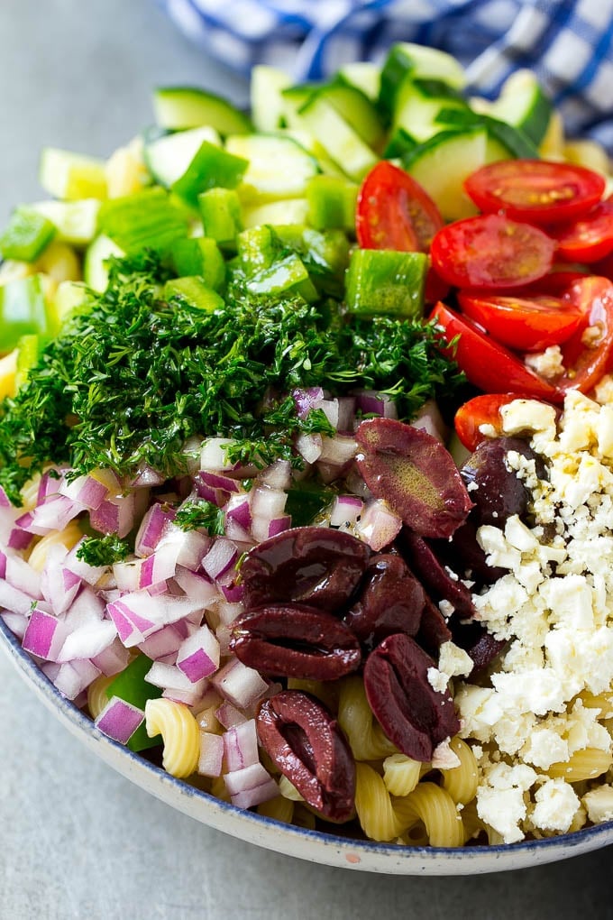 Greek Pasta Salad | Easy Pasta Salad | Vegetable Pasta Salad #pasta #salad #greek #cucumber #tomato #vegetarian #dinner #jonep A bowl of pasta with red onion, kalamata olives, bell pepper and tomatoes, with a drizzle of Greek dressing.