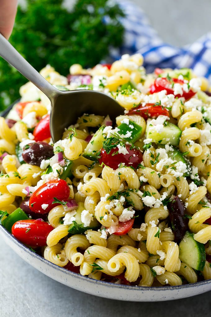 Greek Pasta Salad | Easy Pasta Salad | Vegetable Pasta Salad #pasta #salad #greek #cucumber #tomato #vegetarian #dinner #jonep A bowl of Greek pasta salad with a serving spoon in it.