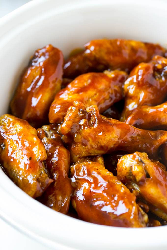 Slow Cooker Barbecue Chicken Wings | Crock Pot Chicken Wings | Barbecue Chicken Wings | Easy Chicken Wings #chickenwings #slowcooker #crockpot #bbqchicken #partywings #appetizer #jonep Slow cooker chicken wings coated in sauce in a white crock pot.
