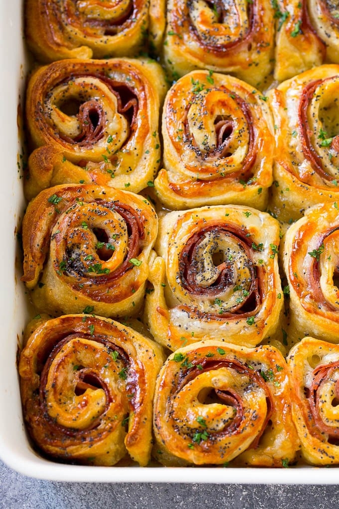 Ham and Cheese Pinwheels Recipe | Ham and Cheese Roll Ups | Ham and Cheese Rolls | Ham and Cheese Bread Rolls #ham #cheese #appetizer #pinwheels #jonep Ham and cheese pinwheels in a baking dish topped with parsley.
