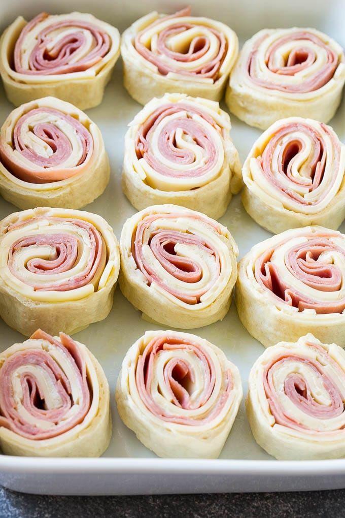 Ham and Cheese Pinwheels Recipe | Ham and Cheese Roll Ups | Ham and Cheese Rolls | Ham and Cheese Bread Rolls #ham #cheese #appetizer #pinwheels #jonep Rolled up ham, cheese and pizza dough circles in a baking dish.