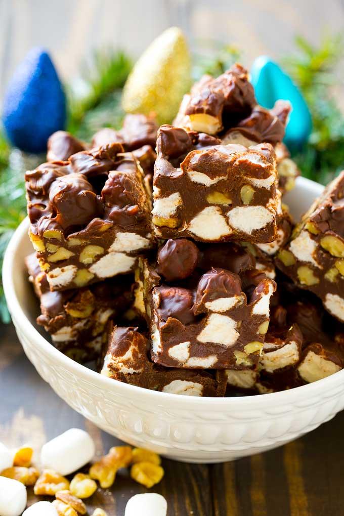 Rocky Road Fudge | Chocolate Marshmallow Fudge | Chocolate Nut Fudge | Microwave Fudge #fudge #chocolatefudge #nobake #chocolate #dessert #rockyroad #jonep A bowl of fudge squares with holiday decorations in the background.