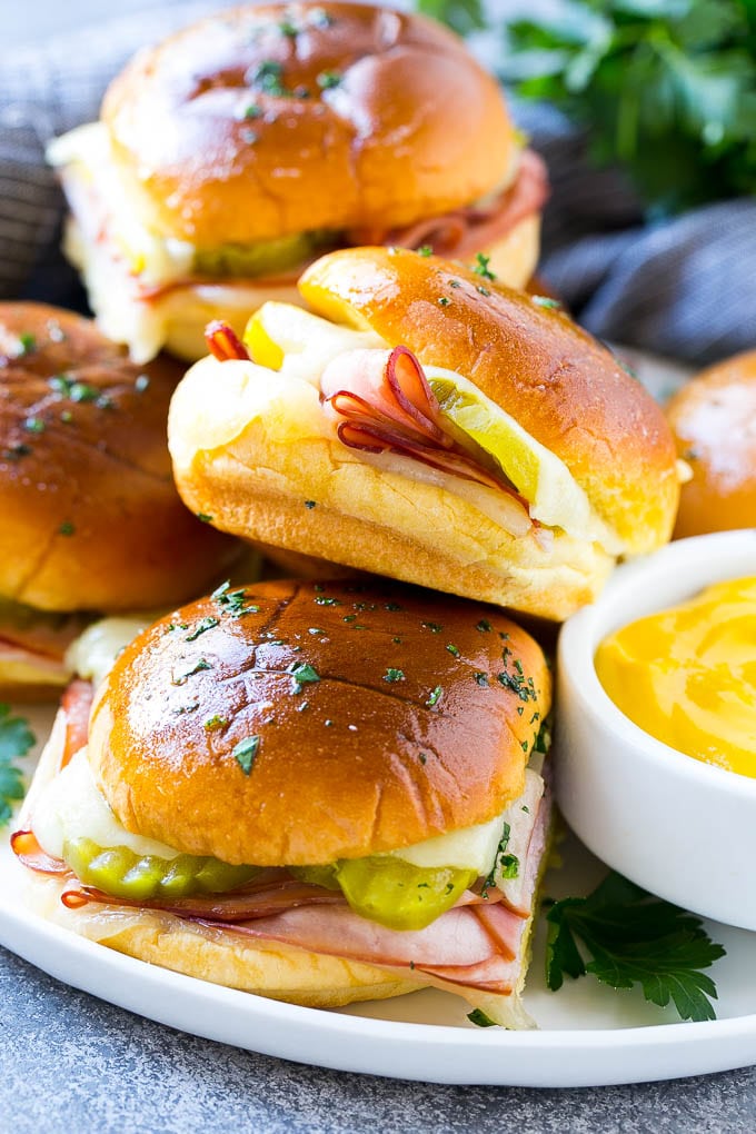 Cuban Sliders Recipe | Cuban Sandwich Recipe | Slider Sandwiches | Ham and Cheese Sliders #sliders #sandwiches #ham #cheese #appetizer #jonep A plate full of Cuban sliders with cheese, pickles and ham on buns.