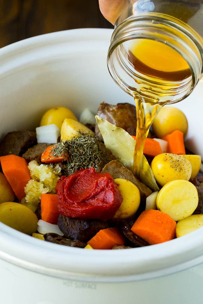Slow Cooker Beef Stew Recipe | Crockpot Beef Stew #stew #soup #beef #slowcooker #crockpot #dinner #jonep Broth being poured into a slow cooker filled with beef and vegetables.