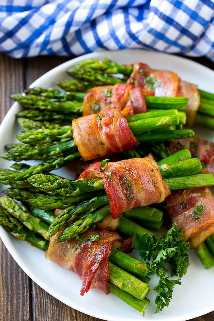Bacon Wrapped Asparagus Recipe | Roasted Asparagus | Asparagus Side Dish #asparagus #bacon #sidedish #dinner #jonep A plate of bacon wrapped asparagus bundles garnished with parsley.