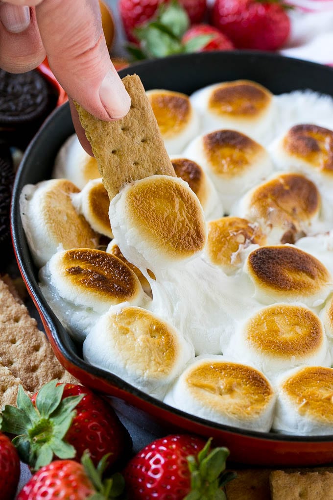 S'mores Dip Recipe | S'mores Skillet | Baked S'mores #smores #dip #chocolate #marshmallow #dessert #jonep A graham cracker topped with melted marshmallow dipping into a skillet of s'mores dip.