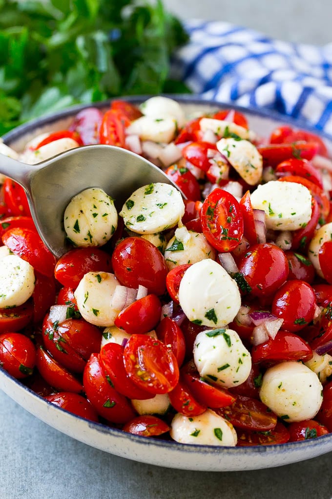 Cherry Tomato Salad Recipe | Tomato Mozzarella Salad | Caprese Salad | Tomato Salad #tomatoes #salad #tomatosalad #caprese #jonep A bowl of cherry tomato salad with a serving spoon in it.