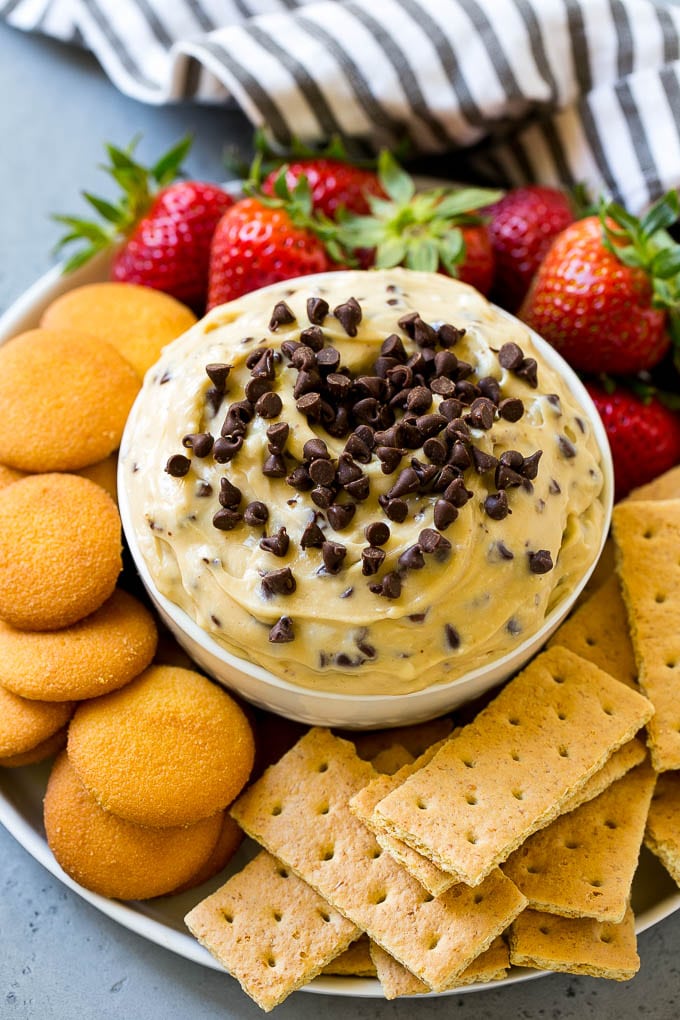 Cookie Dough Dip Recipe | Edible Cookie Dough | Chocolate Chip Cookie Dip #cookies #dip #cookiedough #dessert #snack #jonep A bowl of cookie dough dip topped with chocolate chips and served with cookies and fruit for dipping.