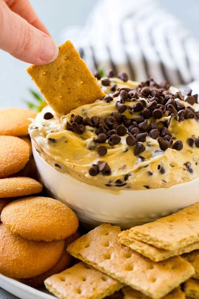 Cookie Dough Dip Recipe | Edible Cookie Dough | Chocolate Chip Cookie Dip #cookies #dip #cookiedough #dessert #snack #jonep A graham cracker dipping into a bowl of cookie dough dip.