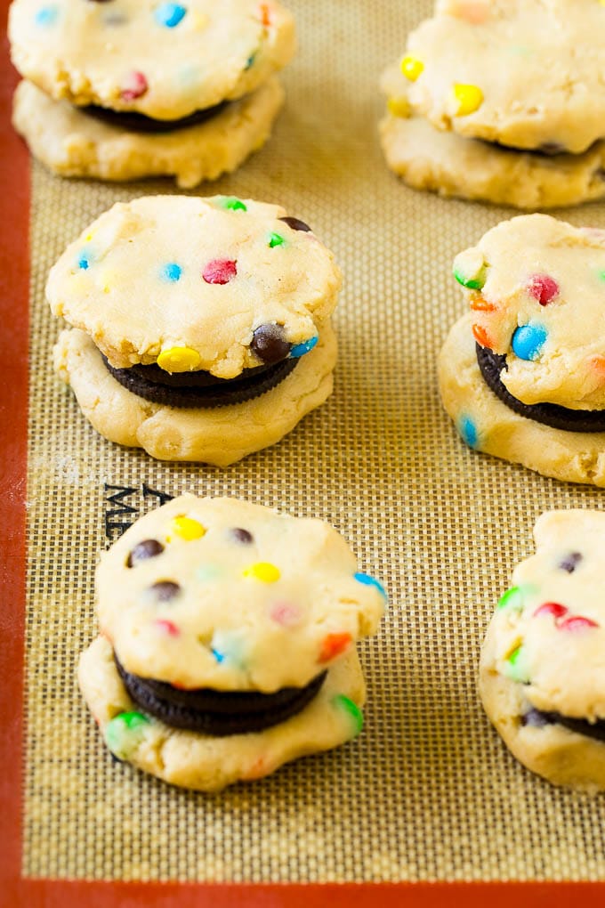 Oreo Stuffed Cookies Recipe | M&M's cookies | Stuffed Cookies #cookies #chocolate #oreos #dessert #baking #jonep Cookie dough sandwiched around Oreos on a baking sheet.