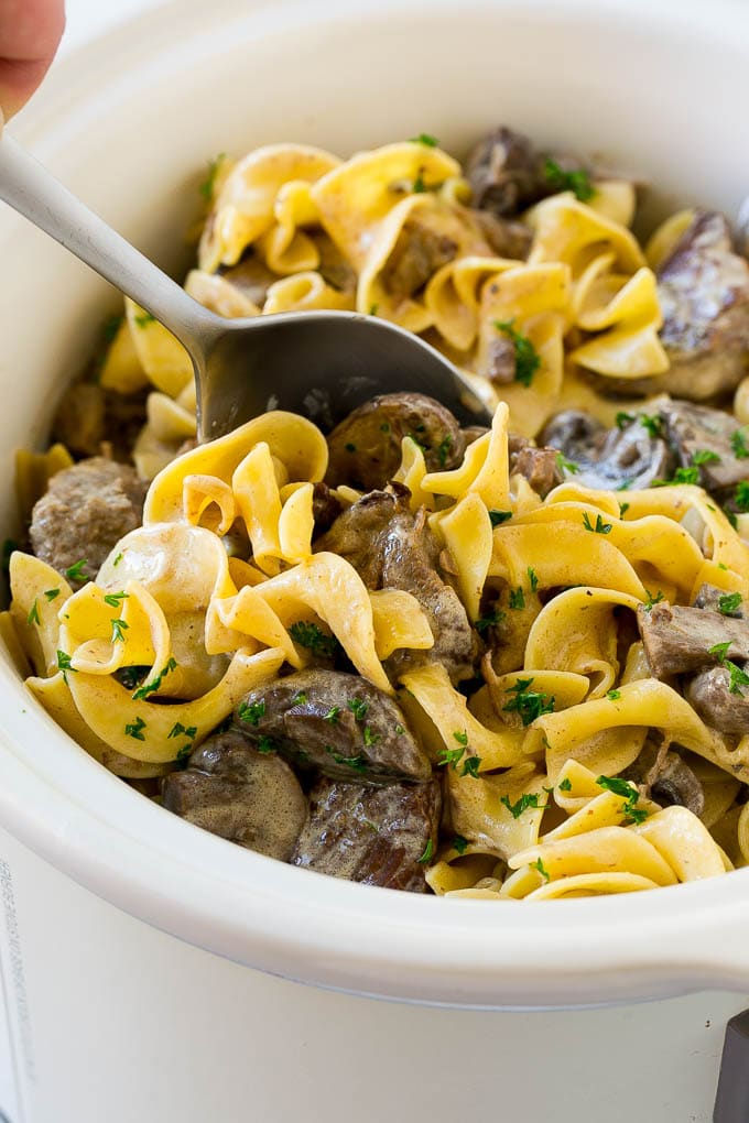 Slow Cooker Beef Stroganoff Recipe | Crock Pot Beef Stroganoff | Beef Recipe #slowcooker #crockpot #beef #mushrooms #pasta #dinner #jonep A crock pot of beef stroganoff with a serving spoon in it.