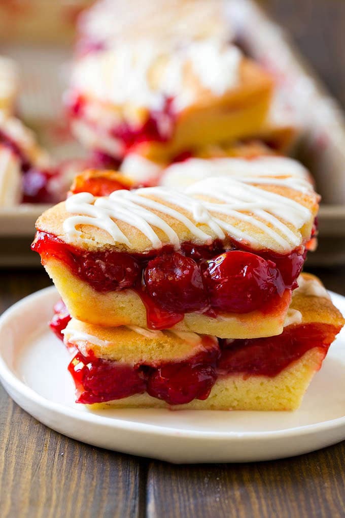 Cherry Bars Recipe | Cherry Pie Bars | Cherry Cookies | Bar Cookies #cookies #bars #cherry #baking #dessert #sweets #jonep Two cherry bars on a plate with a pan of bars in the background.