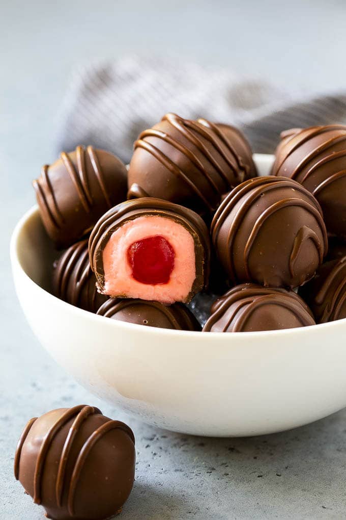 Chocolate Covered Cherries Recipe | Cherry Cordials | Cherry Candy #chocolate #candy #dessert #cherry #sweets #jonep A bowl of chocolate covered cherries with one cut open.