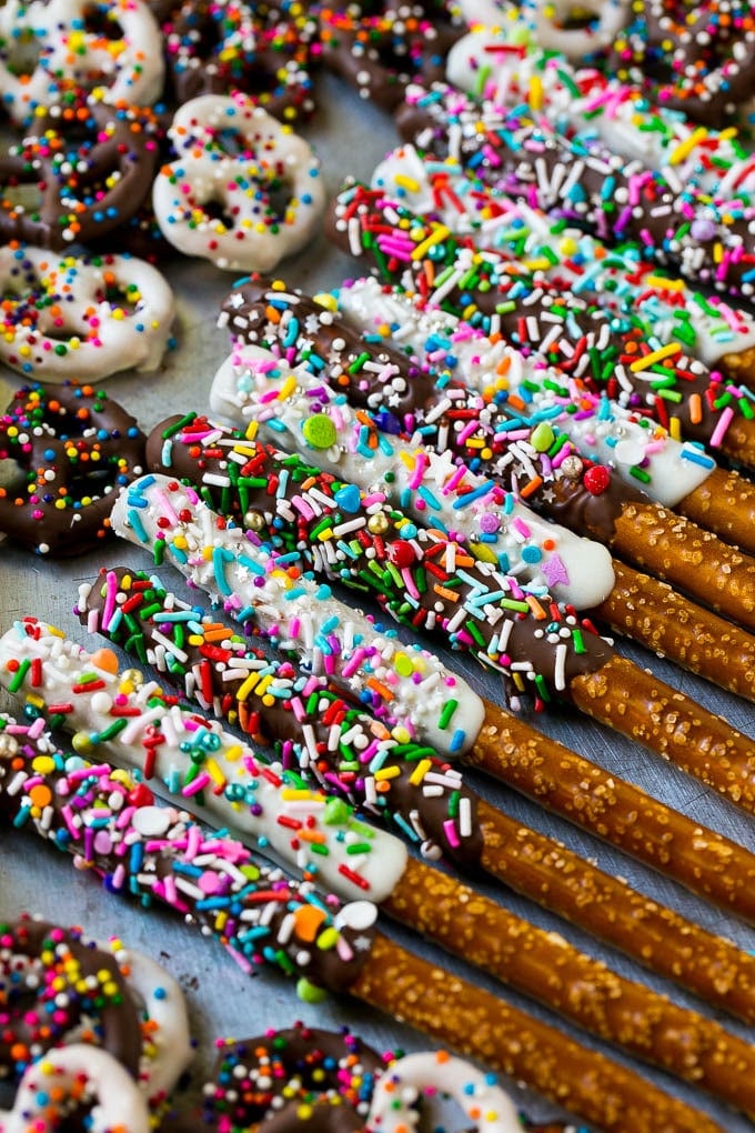 Chocolate Covered Pretzels Recipe | Sprinkle Pretzels | No Bake Dessert #pretzels #chocolate #christmas #sprinkles #candy #jonep A sheet pan with coated twists and rods decorated with rainbow sprinkles.