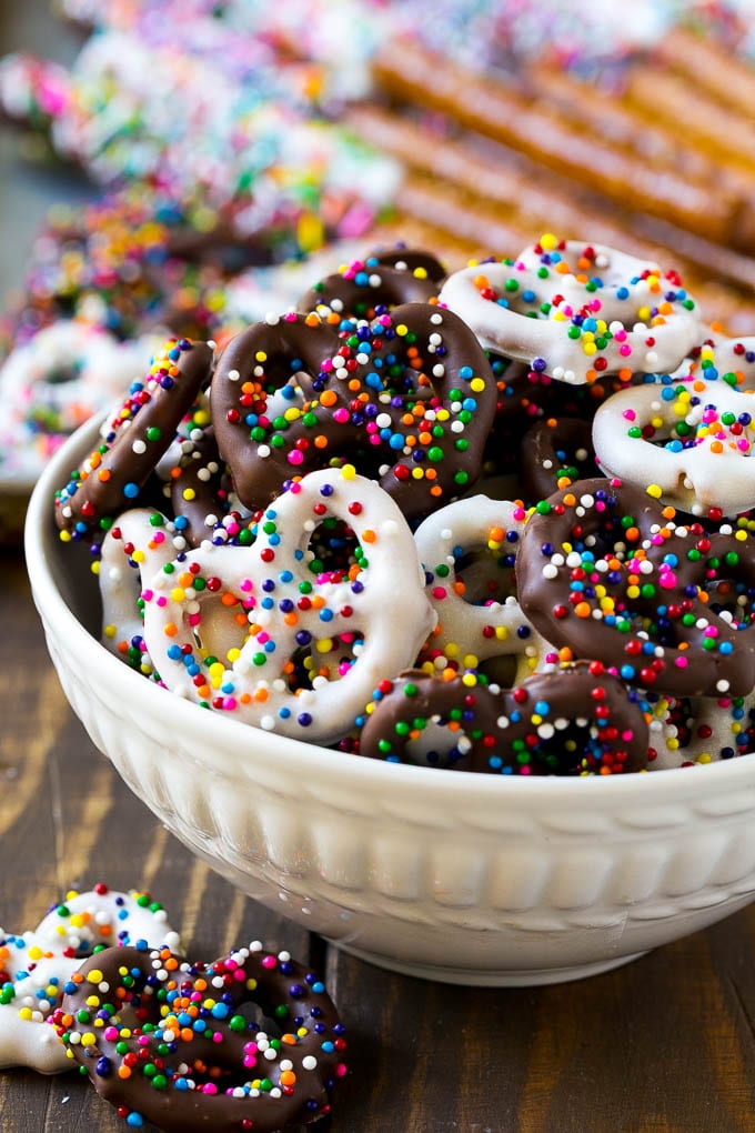 Chocolate Covered Pretzels Recipe | Sprinkle Pretzels | No Bake Dessert #pretzels #chocolate #christmas #sprinkles #candy #jonep A bowl of chocolate covered pretzels decorated with rainbow sprinkles.