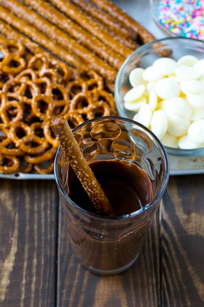 Chocolate Covered Pretzels Recipe | Sprinkle Pretzels | No Bake Dessert #pretzels #chocolate #christmas #sprinkles #candy #jonep A rod in a glass full of melted chocolate.