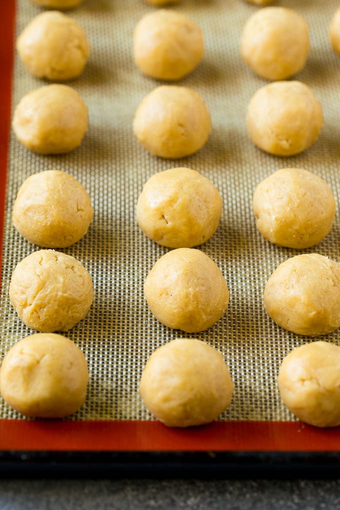 Peanut Butter Blossoms Recipe | Hershey Kiss Cookies | Chocolate Peanut Butter Cookies #cookies #peanutbutter #chocolate #dessert #baking #christmas #christmascookies #jonep Balls of dough on a baking sheet.