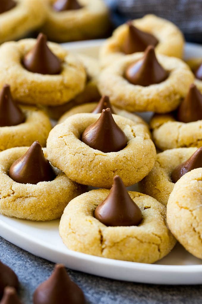 Peanut Butter Blossoms Recipe | Hershey Kiss Cookies | Chocolate Peanut Butter Cookies #cookies #peanutbutter #chocolate #dessert #baking #christmas #christmascookies #jonep A plate with peanut butter blossoms stacked onto it.