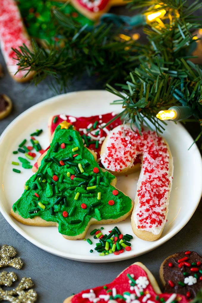 Christmas Sugar Cookies Recipe | Christmas Cookies #cookies #frosting #sprinkles #sugarcookies #christmas #dessert #jonep A selection of Christmas sugar cookies served on a plate, with holiday decorations in the background.