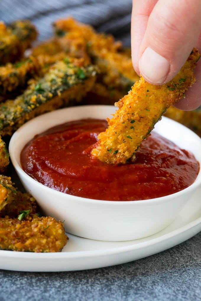 Fried Zucchini Recipe | Zucchini Fries | Zucchini Recipe #appetizer #zucchini #snack #jonep A hand dipping a piece of fried zucchini into marinara sauce.