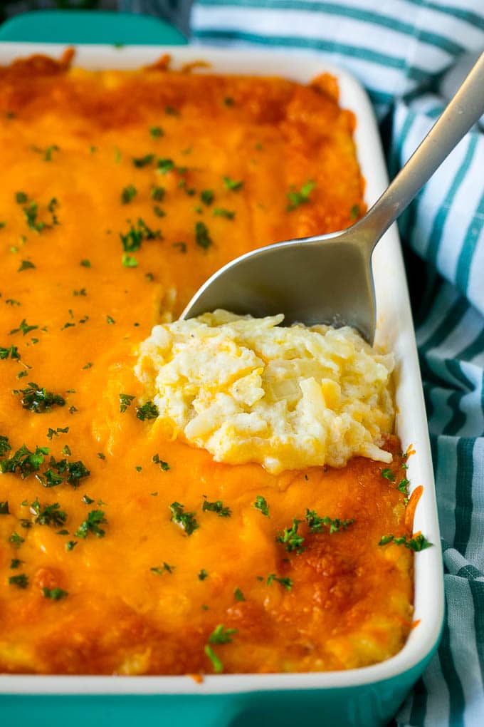 Hash Brown Casserole | Potato Casserole | Hash Brown Side Dish #potatoes #cheese #casserole #sidedish #jonep Hash brown casserole with potatoes, cheddar cheese, onions and sour cream, with a serving spoon in the dish.
