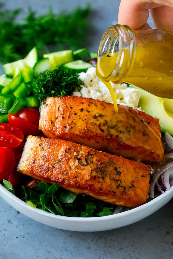 Greek Salmon Salad Recipe | Low Carb Salmon Recipe | Salmon Salad #salmon #seafood #fish #lowcarb #keto #lunch #jonep #healthy Salmon fillets on top of greens with dressing being poured over the top.