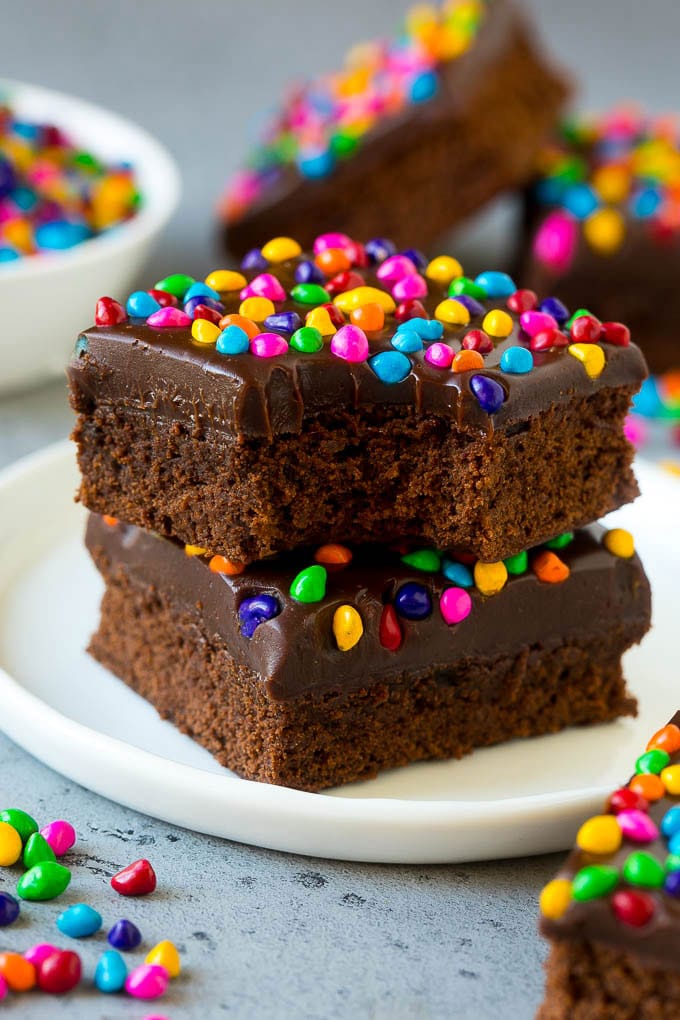 Cosmic Brownies Recipe | Cocoa Brownies | Frosted Brownies #brownies #chocolate #dessert #jonep #sprinkles A stack of cosmic brownies on a plate with a bite taken out of one.
