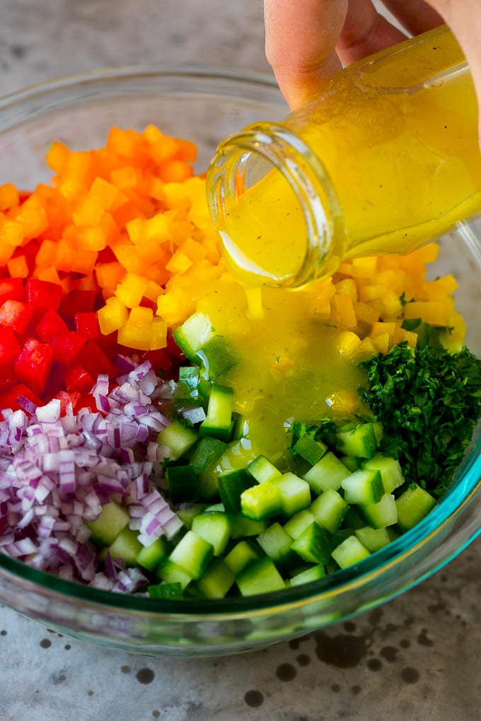 Israeli Salad Recipe | Cucumber Salad | Tomato Salad | Chopped Salad #salad #cleaneating #healthy #glutenfree #lowcarb #keto #sidedish #lunch #jonep Lemon dressing being poured over chopped vegetables.