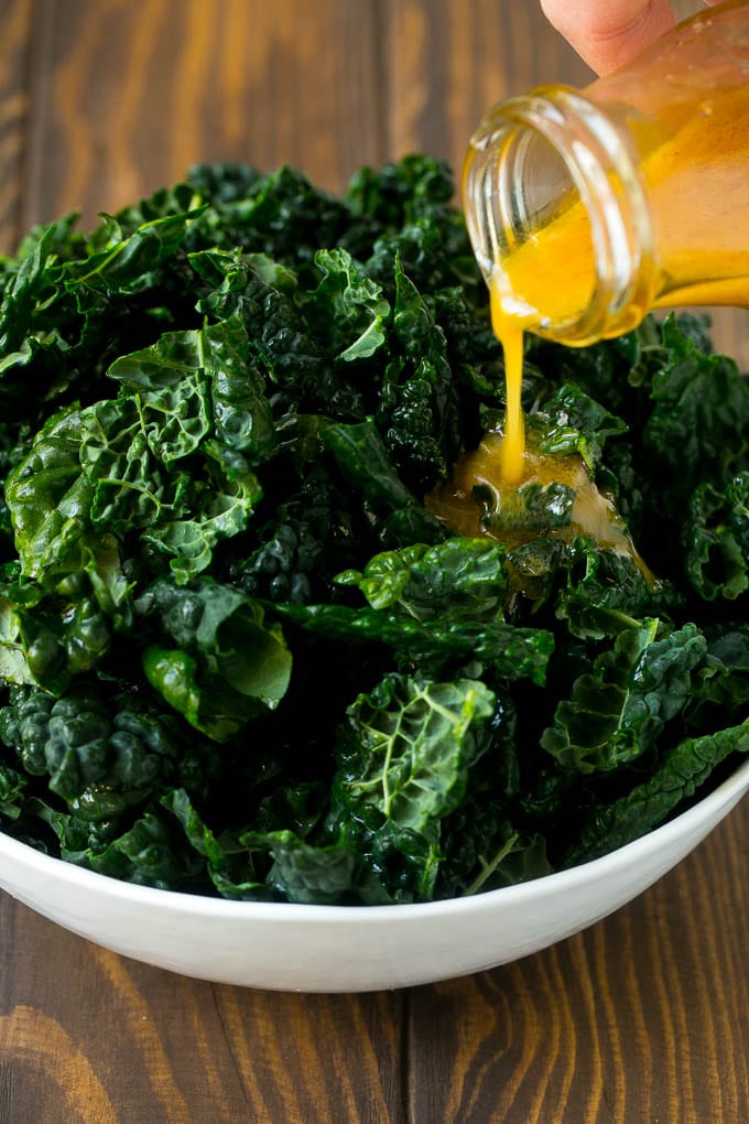 Apple Kale Salad Recipe | Kale Recipe | Fall Salad #kale #apples #bacon #salad #feta #dinner #lunch #jonep Dressing being poured over dinosaur kale leaves.
