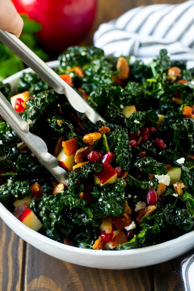Apple Kale Salad Recipe | Kale Recipe | Fall Salad #kale #apples #bacon #salad #feta #dinner #lunch #jonep Tongs in a bowl of kale and apple salad.