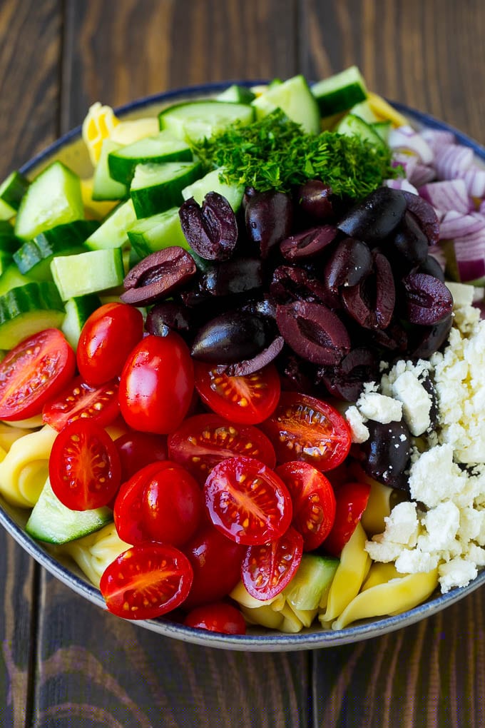 Greek Tortellini Salad Recipe | Pasta Salad | Tortellini Salad | Greek Salad #greek #tortellini #pasta #salad #cucumbers #olives #dinner #jonep Tortellini in a bowl topped with olives, tomatoes, cucumber and feta cheese.