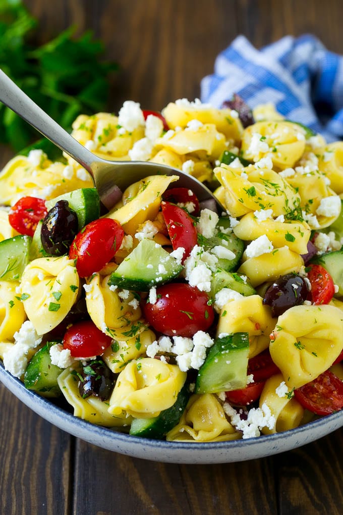 Greek Tortellini Salad Recipe | Pasta Salad | Tortellini Salad | Greek Salad #greek #tortellini #pasta #salad #cucumbers #olives #dinner #jonep A bowl of Greek tortellini salad with a serving spoon in it.