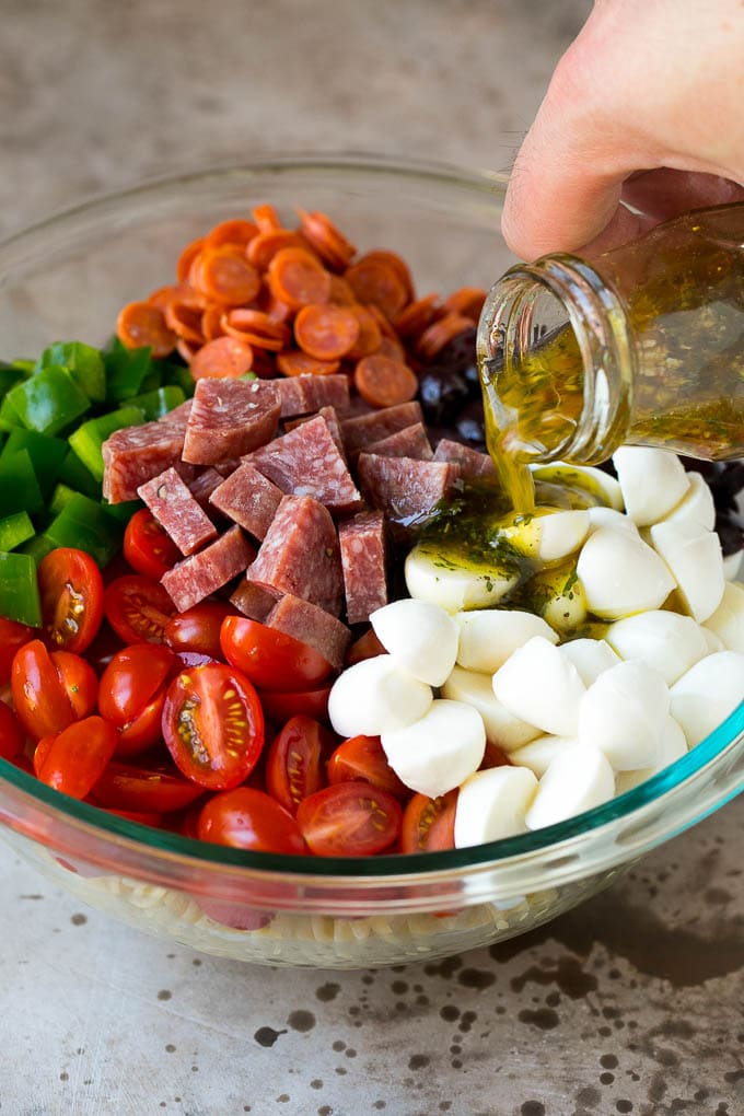 Italian Pasta Salad | Pasta Salad Recipe #pasta #salad #pastasalad #pepperoni #salami #olives #cheese #sidedish #jonep Italian dressing being poured over pasta salad ingredients.