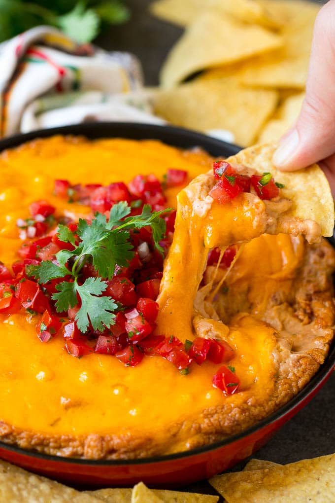 Bean Dip Recipe | Mexican Dip #dip #appetizer #mexicanfood #beans #cheese #jonep A tortilla chip scooping out a serving of Mexican bean dip.