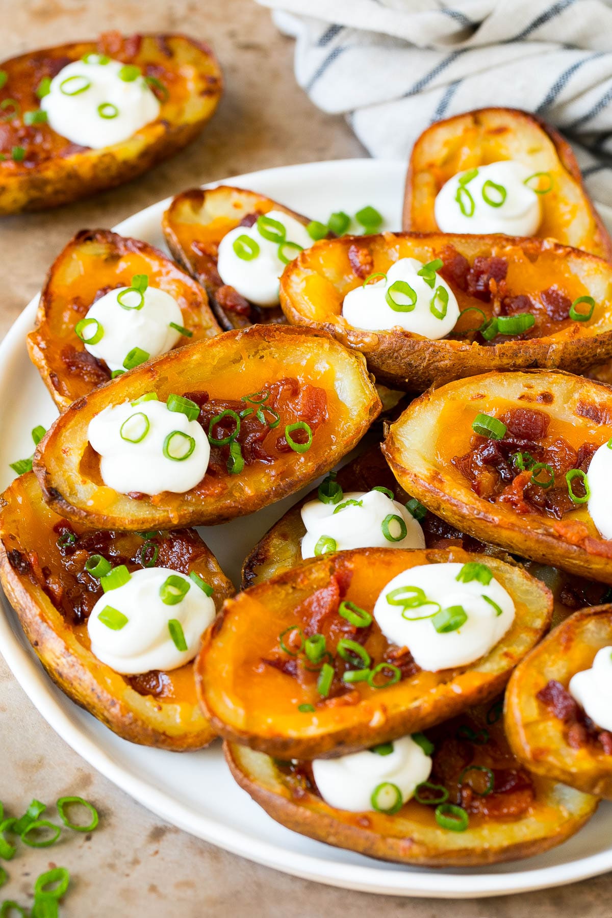 Potato Skins Recipe | Loaded Potatoes #potatoes #appetizer #snack #cheese #bacon #jonep A serving plate of potato skins topped with bacon and sour cream.