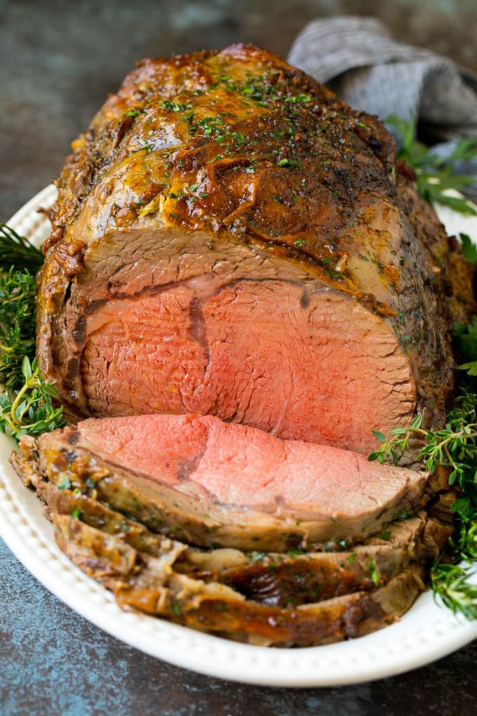 Prime Rib Recipe #primerib #beef #roast #dinner #thanksgiving #christmas #keto #lowcarb #jonep A sliced slow roasted prime rib roast surrounded by fresh herbs.