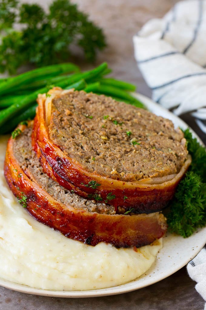 Bacon Wrapped Meatloaf Recipe | Beef Meatloaf #meatloaf #beef #groundbeef #bacon #dinner #jonep Slices of bacon wrapped meatloaf served over mashed potatoes with green beans.
